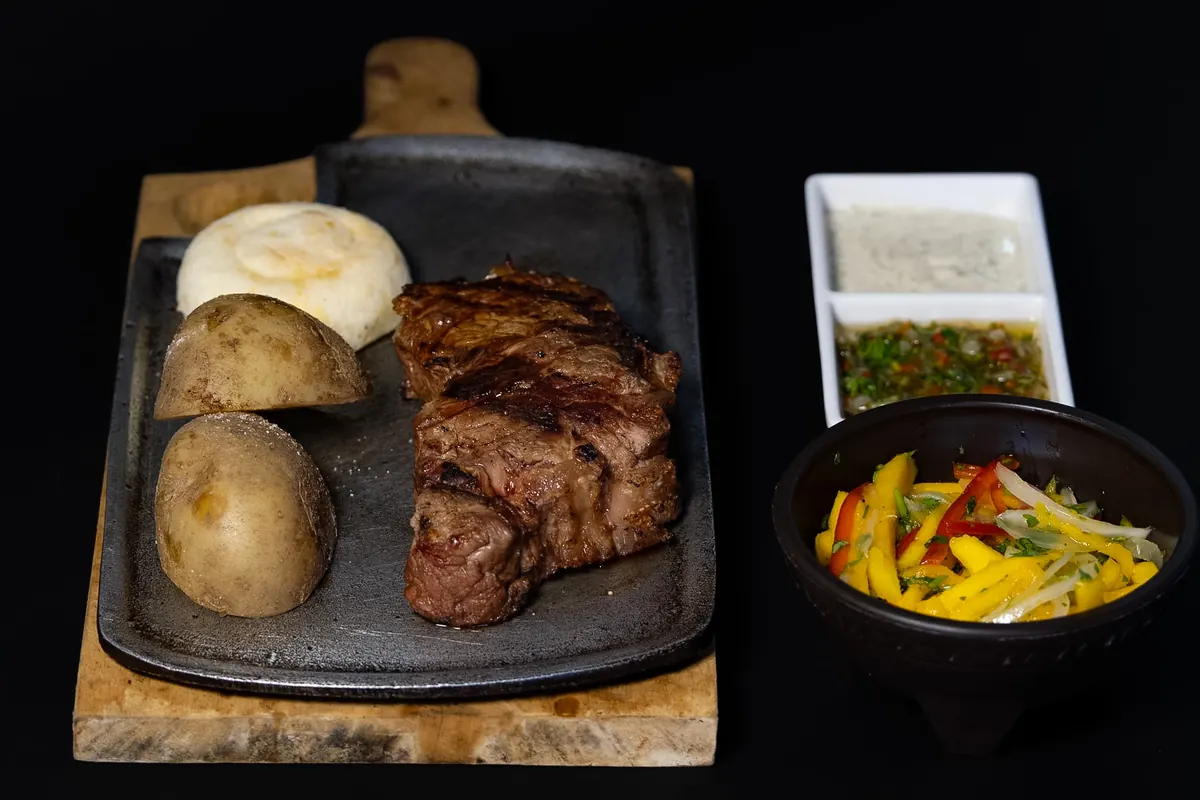 Churrasco a la parrilla con papas, arepa, chimichurri y ensalada de mango
