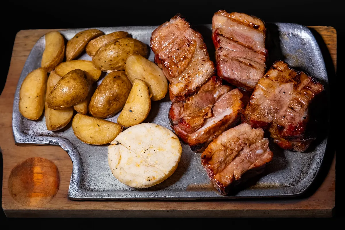 Costillas al barril servidas en tabla de hierro con papas en cascos y arepa