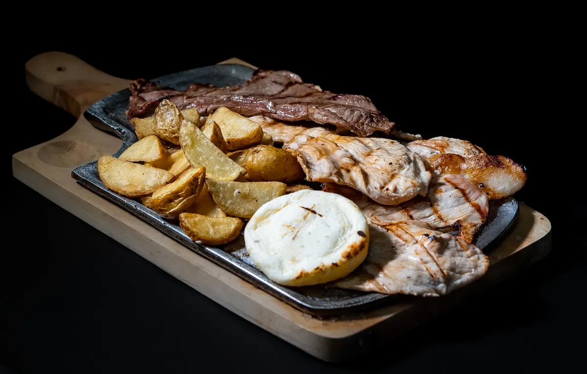 Plato mixto de res y pollo a la parrilla con papas en cascos y arepa